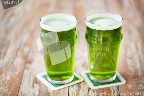 Image of two glasses of green beer on wooden table