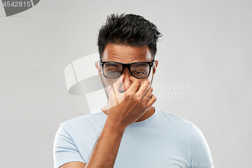 Image of tired indian man in glasses rubbing nose bridge