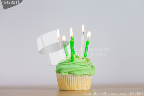 Image of green cupcake with six burning candles on table