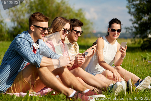 Image of smiling friends with smartphones sitting on grass