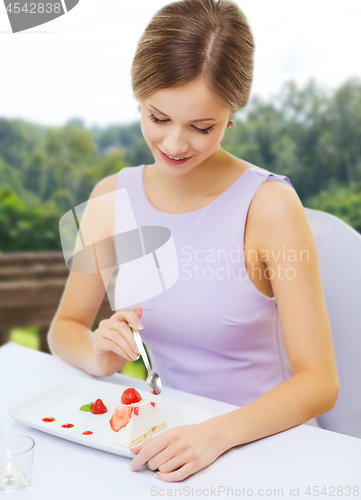 Image of smiling young woman eating dessert at restaurant