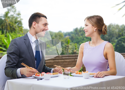 Image of smiling couple eating sushi rolls at restaurant