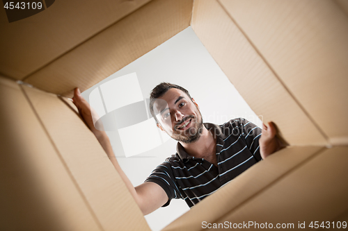 Image of Man smiling, unpacking and opening carton box and looking inside