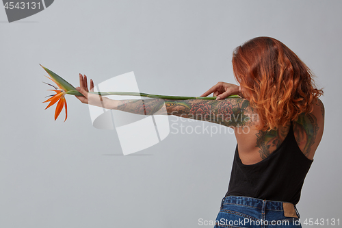 Image of View from the back of a girl with a tattoo with an orange flower strelitzia on a gray background with copy space for text.