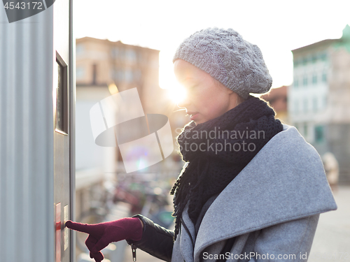 Image of Casual woman buying public transport tickets on city urban vedning machine on cold winter day.