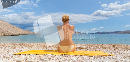 Image of Rear view of sexy young caucasian woman sunbathing topless on romote pabble beach on Pag island, Croatia, Mediterranean.