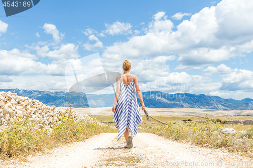 Image of Rear view of woman in summer dress holding bouquet of lavender flowers while walking outdoor through dry rocky Mediterranean Croatian coast lanscape on Pag island in summertime