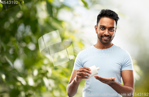 Image of happy indian man applying lotion to his hand