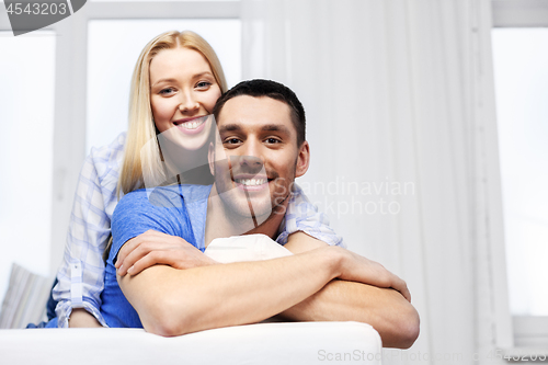 Image of happy couple sitting on sofa and hugging at home