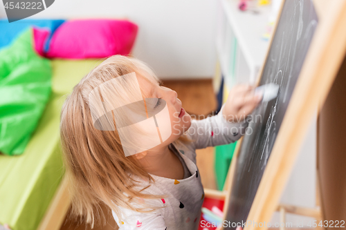 Image of happy little girl drawing on chalk board at home