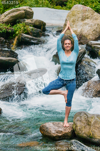 Image of Woman in yoga asana Vrikshasana tree pose at waterfall outdoors