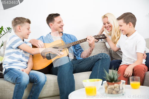 Image of Happy caucasian family smiling, playing guitar and singing songs together at cosy modern home