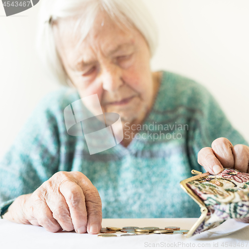 Image of Concerned elderly woman sitting at the table counting money in her wallet.