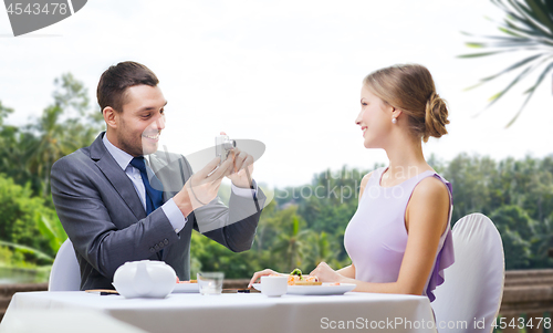 Image of man photographing woman by camera at restaurant