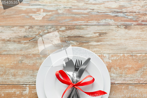 Image of cutlery tied with red ribbon on set of plates