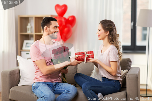 Image of happy man giving woman flowers and present at home