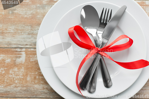 Image of cutlery tied with red ribbon on set of plates