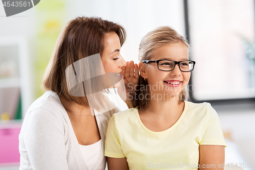 Image of happy mother whispering secret to daughter at home