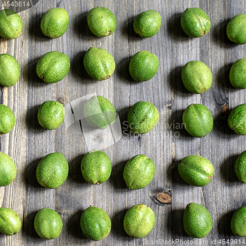 Image of Young green fruits of walnuts lie in rows on a gray wooden background.