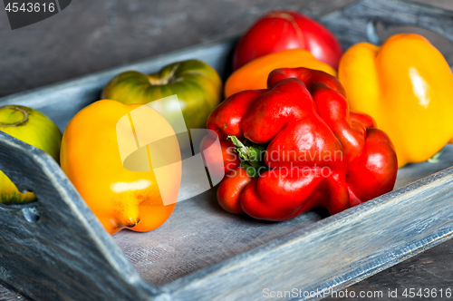 Image of Imperfect natural peppers and tomatoes on an old wooden tray on a dark background. Healthy eating concept.