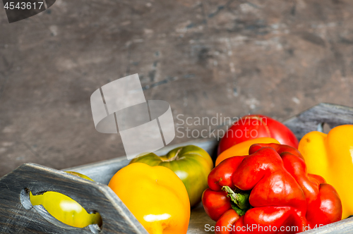 Image of Imperfect natural peppers and tomatoes on an old wooden tray on a dark background. Copy Space.