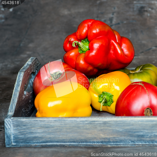 Image of Imperfect natural peppers and tomatoes on an old wooden tray on a dark background. Healthy eating concept.