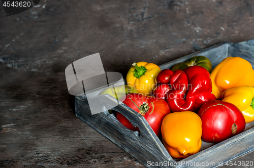 Image of Imperfect natural peppers and tomatoes on an old wooden tray on a dark background. Copy Space.