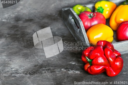 Image of Imperfect natural peppers and tomatoes on an old wooden tray on a dark background. Copy Space.