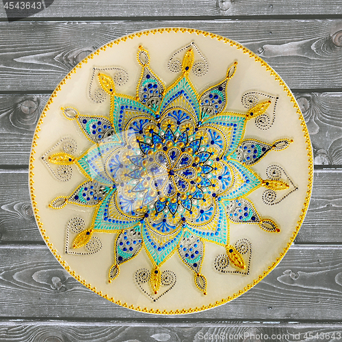 Image of Decorative ceramic plate, hand painted dot pattern with acrylic paints on a gray wooden background. A square photo. Closeup.