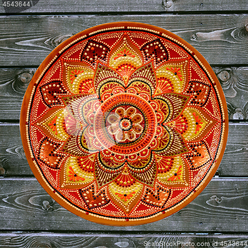 Image of Decorative ceramic plate, hand painted dot pattern with acrylic paints on a gray wooden background. A square photo. Closeup.