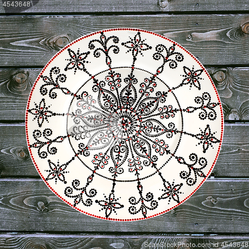 Image of Decorative ceramic plate, hand painted dot pattern with acrylic paints on a gray wooden background. A square photo. Closeup.