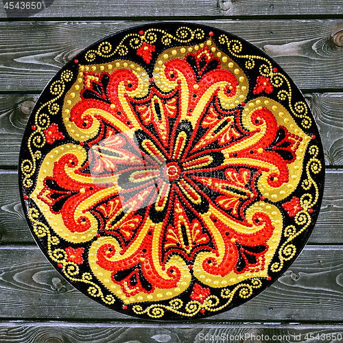 Image of Decorative ceramic plate, hand painted dot pattern with acrylic paints on a gray wooden background. A square photo. Closeup.