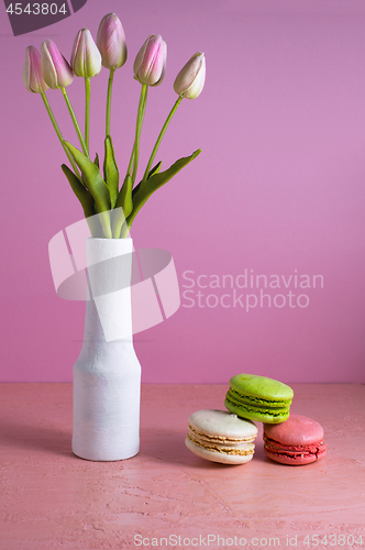 Image of Macaroons on a pale pink background next to a vase of tulips. Place for text.