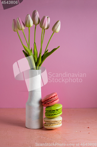 Image of Macaroons on a pale pink background next to a vase of tulips. Place for text.