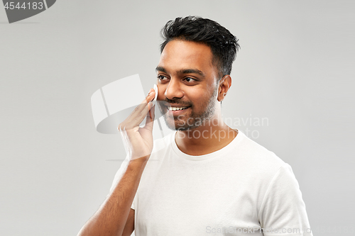 Image of smiling indian man cleaning face with cotton pad