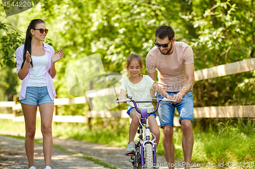 Image of kid with patents learning to ride bicycle in park