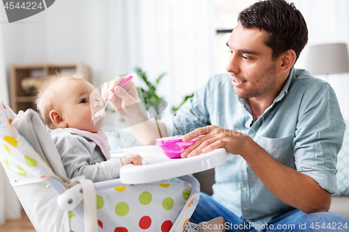 Image of father feeding happy baby in highchair at home