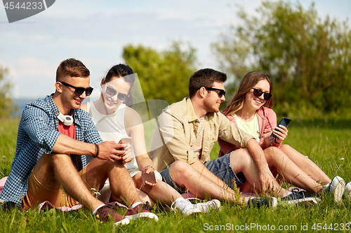 Image of smiling friends with smartphones sitting on grass