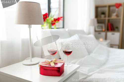 Image of gift and two glasses of wine in bedroom at home