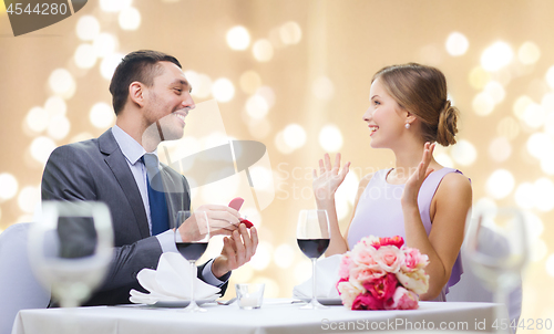 Image of man giving woman engagement ring at restaurant