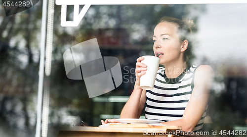 Image of Young caucasian woman sitting alone in coffee shop thoughtfully leaning on her hand, looking trough the window