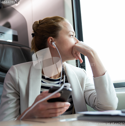 Image of Thoughtful businesswoman listening to podcast on mobile phone while traveling by train.