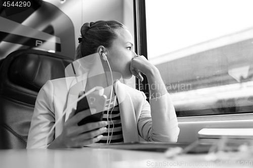 Image of Thoughtful businesswoman listening to podcast on mobile phone while traveling by train.