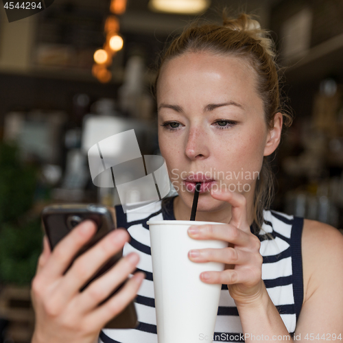 Image of Thoughtful woman reading news on mobile phone while sipping coffee in coffee shop.