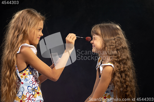 Image of Girl powdering nose to her sister, sister squinting from tickling