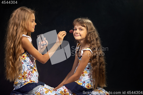 Image of The older sister is applying powder to the younger girl\'s face