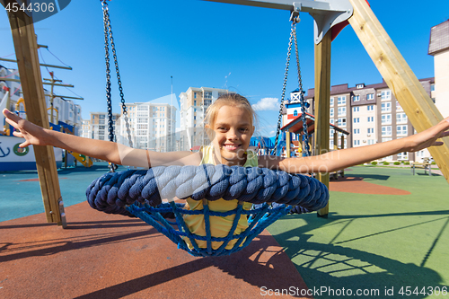 Image of Girl joyfully spread her arms while riding on a round hanging swing