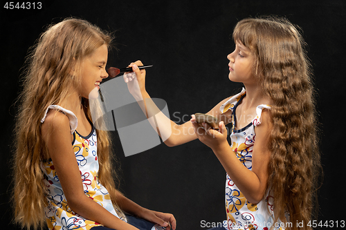 Image of Girl powdering with a brush a nose to another girl, studio, black background