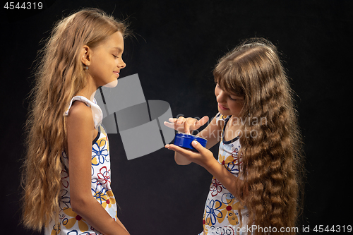 Image of A girl puts jar cream on her finger, another girl sits nearby