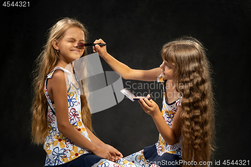 Image of The girl closed her eyes when another girl powder her nose with a brush